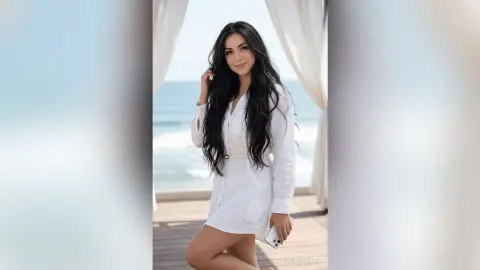 Smiling woman in a white linen shirt relaxing on a breezy seaside balcony overlooking the ocean.