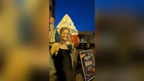 Smiling blonde woman in a black satin dress at an evening outdoor breakfast buffet event in Berlin.