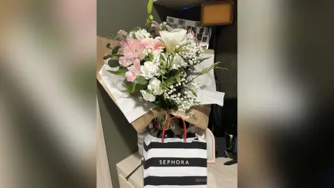 Beautiful bouquet of pink lilies and white baby's breath flowers in a gift bag on a wooden table.
