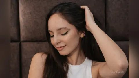 LeahEvans with long dark hair and winged eyeliner posing in a white tank top.