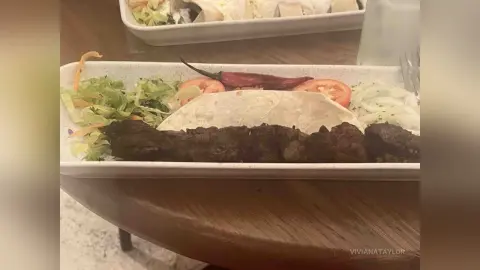 Delicious grilled meat wrap with fresh salad and tomato served in a white takeout container on a wooden table.
