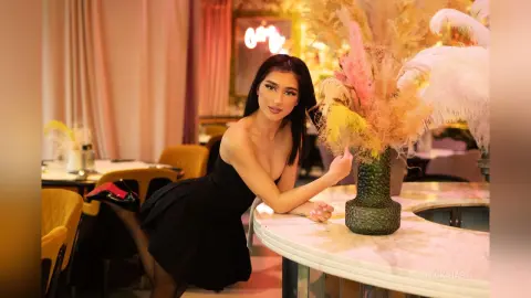 Elegant woman in a black cocktail dress leaning on a marble table in a chic, warm-lit restaurant setting.