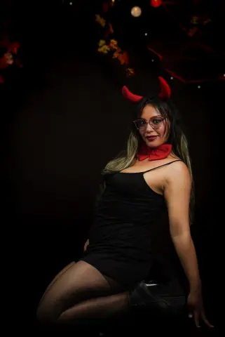 Woman in a black dress and red devil horns posing against a dark background for a spooky Halloween mood.