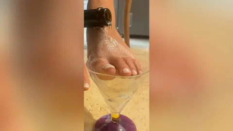 FelishaRose dangles her bare foot over a clear martini glass filled with liquid.
