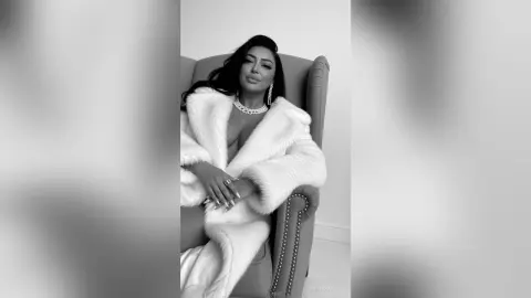 Glamorous woman in a white faux fur robe and diamond jewelry sitting in a luxury armchair.