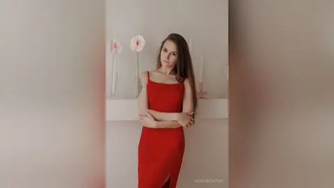 IngridBeckton poses in a red dress with her arms crossed against a white wall with pink flowers.