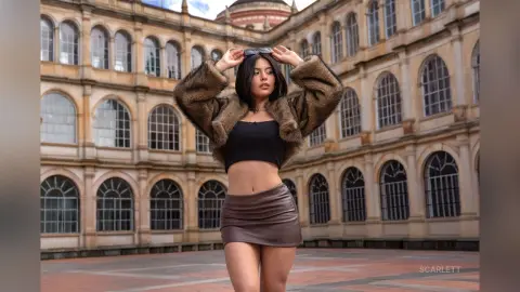 Stylish woman in a brown faux fur jacket and black crop top posing in a historic European courtyard.