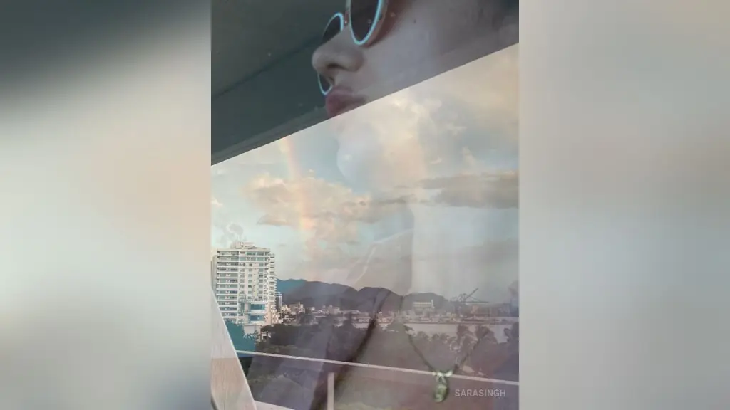 SaraSingh — Young woman in sunglasses looking at a city skyline view from a high-rise balcony during sunset.
