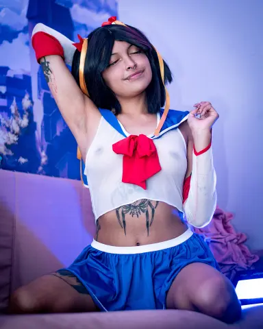 SakuraTao poses with one arm up, wearing a white and blue sailor outfit that shows her nipples, black hair, and stomach tattoos.