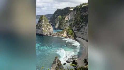 Scenic view of turquoise ocean waves crashing against steep limestone cliffs in a tropical coastal landscape.