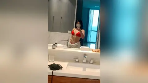 Young woman in a red bikini taking a mirror selfie in a modern, bright bathroom.