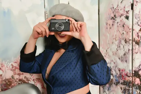 Stylish woman in a blue blazer and beret holding a vintage camera against a floral background.