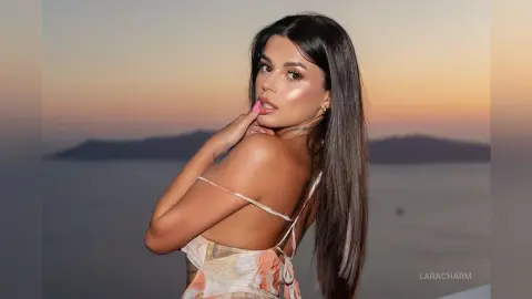 Glamorous woman in a floral slip dress posing during a sunset at a seaside resort.
