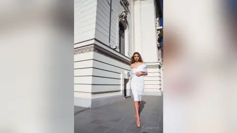 Elegant woman in a white cocktail dress posing in front of a classic white building on a sunny day.