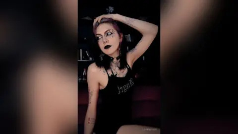 LorenLoiss poses with one hand behind her head, wearing a black tank top and dark lipstick with heavy eye makeup.