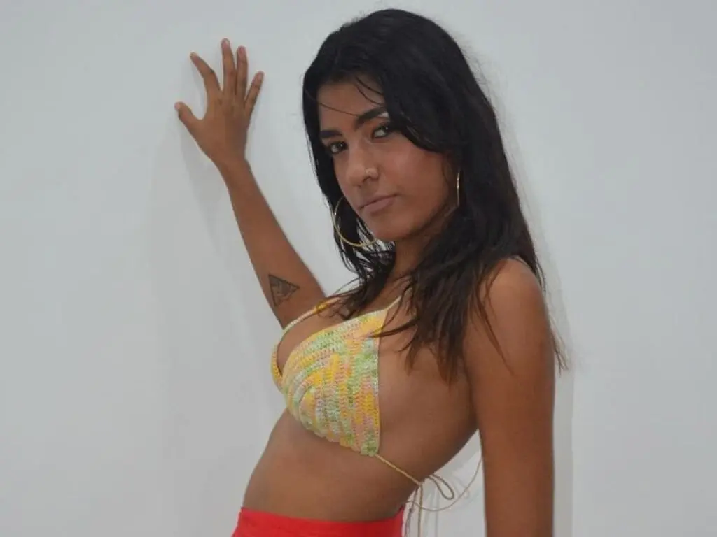 Young woman in a yellow crochet bikini top posing against a white wall with a relaxed summer mood.