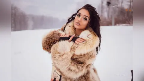 Glamorous woman in a luxury faux fur coat posing in a snowy winter landscape.