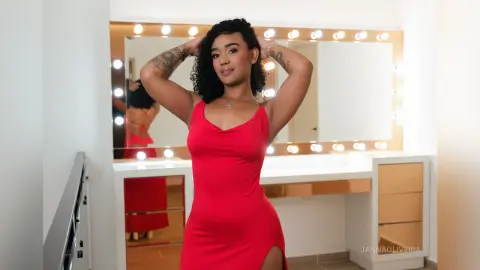 Young woman with curly hair in a red cocktail dress posing in a bright makeup studio with vanity lights.