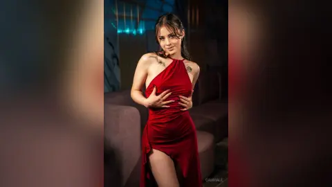 Elegant woman in a red halter dress posing in a moody, dimly lit lounge setting.