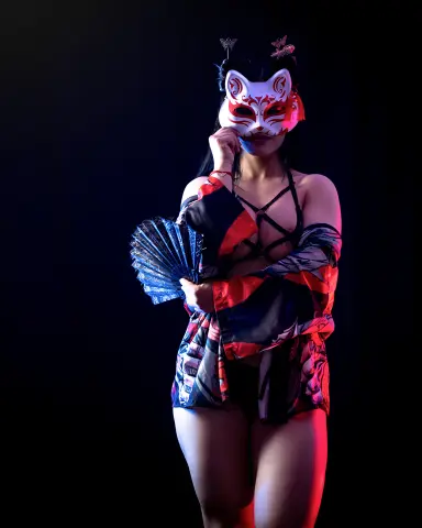 Woman in red kimono and Kitsune mask holding a blue fan against a dark studio background.