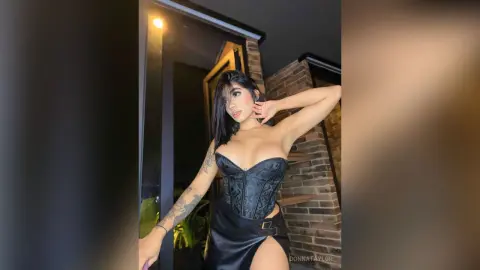 Glamorous woman in a black lace corset and leather skirt posing in a modern dimly lit interior.