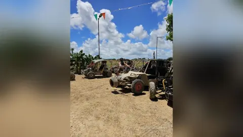RossiNoleen sits in a tan off-road buggy parked on a dirt path under a blue sky with white clouds.