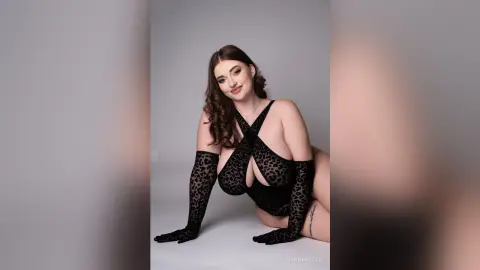 Curvy woman in a black leopard print bodysuit and matching gloves posing confidently against a grey studio background.