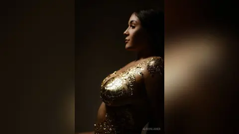 Side profile of a woman in a shimmering gold sequin dress against a dark, moody background.