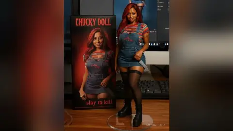 Woman in denim overall dress and black tights standing next to a Chucky Doll collector box in a studio setting.