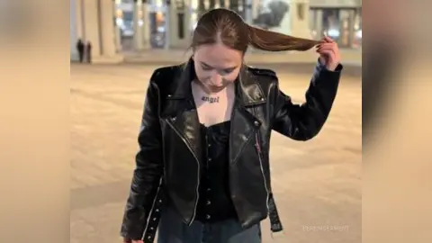 Young woman in a black leather jacket and dark top posing outdoors at night with a cool, edgy vibe.
