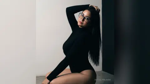Stylish woman in a black long-sleeve bodysuit posing against a minimalist white wall for a moody portrait.