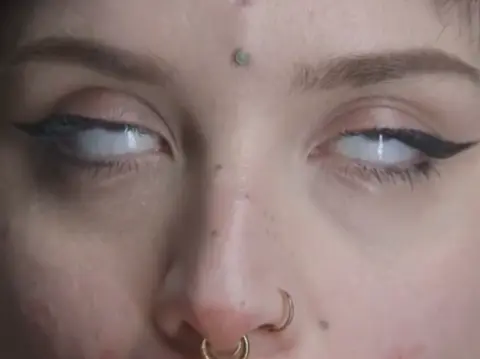 Close-up of a woman with dramatic winged eyeliner, a nose ring, and a forehead bindi in a moody portrait.