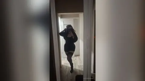 Woman in a black outfit posing in a doorway for a moody indoor mirror selfie.