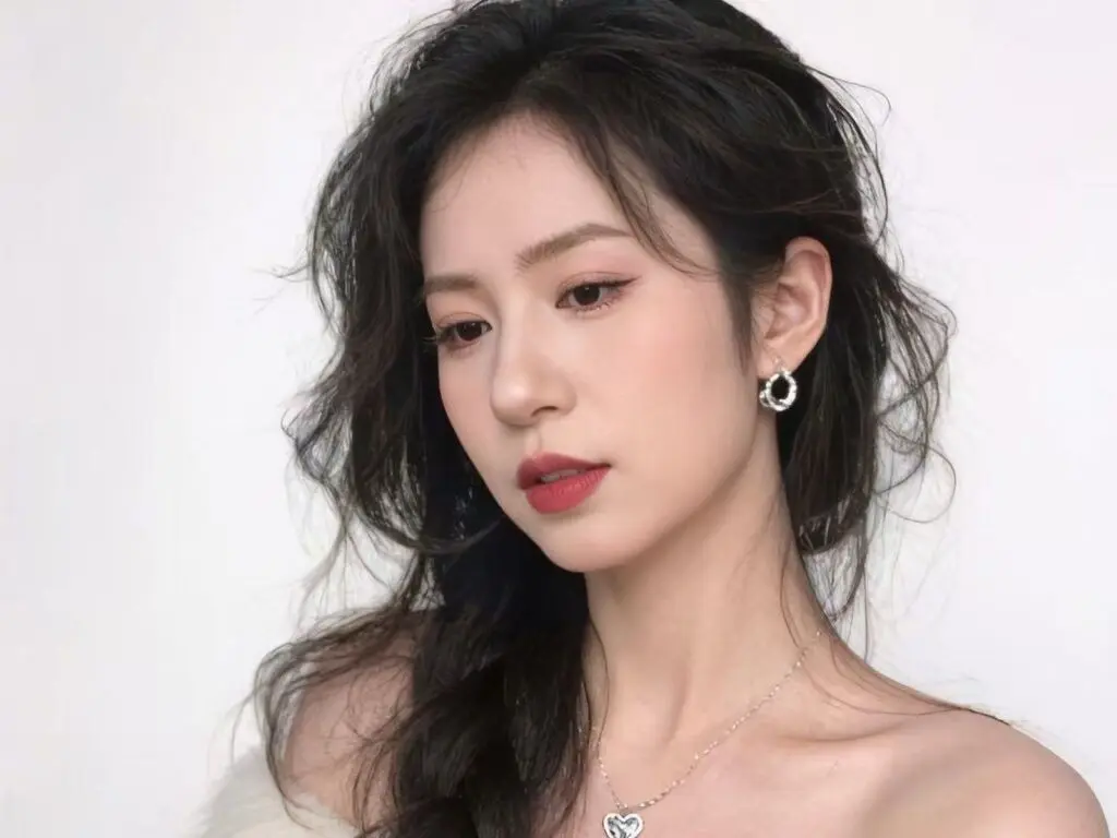 Elegant woman with wavy dark hair and silver hoop earrings posing against a clean white background.