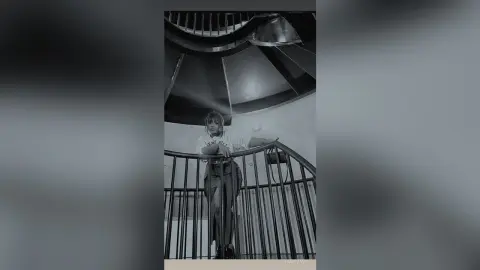 Stylish woman in a white graphic t-shirt and dark trousers posing on a modern spiral staircase in black and white.