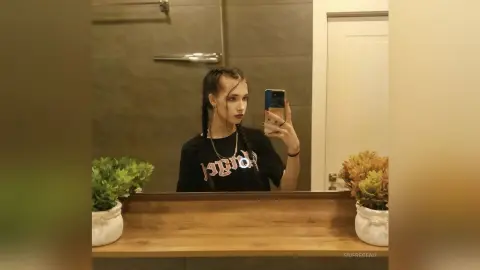 Young woman in a black graphic t-shirt taking a mirror selfie in a modern bathroom setting.