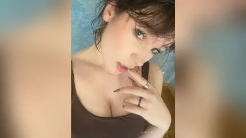 Young woman with dark hair in a black tank top posing with a thoughtful expression against a blue background.