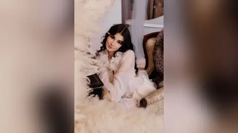 Elegant woman in a white flowing blouse sitting in a dreamy, soft-lit vintage room.