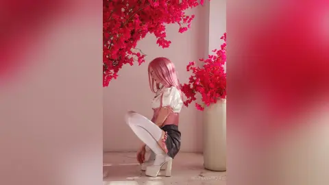 Woman with pink hair in a white blouse and dark skirt posing amidst vibrant pink bougainvillea flowers.