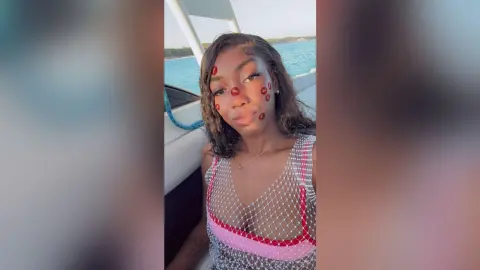 NatyGlow wearing a white mesh tank top while sitting on a boat overlooking the blue ocean water.