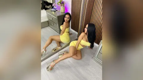 Glamorous woman in a yellow two-piece outfit sitting on a floor in a modern bedroom setting.