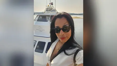 Smiling woman in white outfit and sunglasses relaxing on a luxury boat during a sunny day trip.