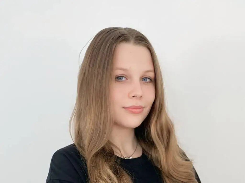 Young woman with long blonde hair wearing a black t-shirt against a plain white background.
