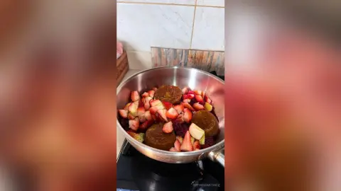 Fresh sliced strawberries and golden baked fruit muffins in a stainless steel pan on a kitchen stovetop.
