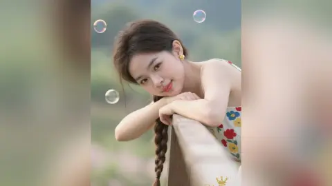 Smiling young woman in a floral sundress leaning on a wooden railing amidst floating bubbles in a soft garden setting.