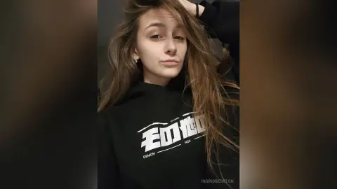 IngridBeckton poses wearing a black hoodie with white text, letting her long brown hair fall over her shoulders.
