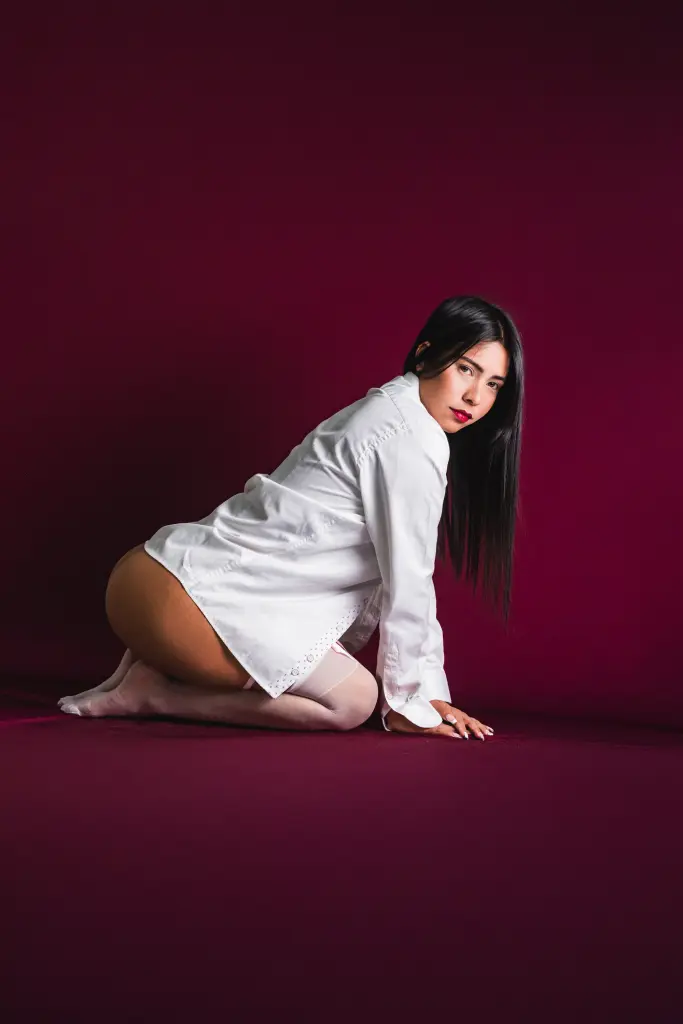 VelvetRosss poses in a black tank top and patterned black tights against a deep purple background.