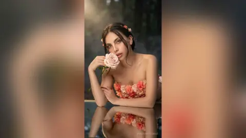 Elegant woman in a floral pink strapless dress holding a rose in a soft, romantic garden setting.