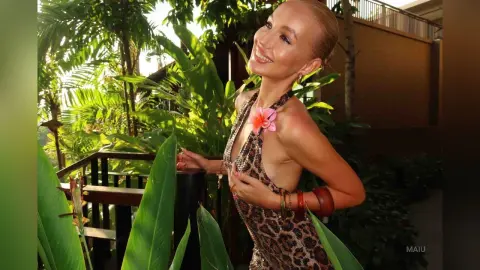 Smiling blonde woman in a leopard print dress enjoying a sunny tropical garden setting.