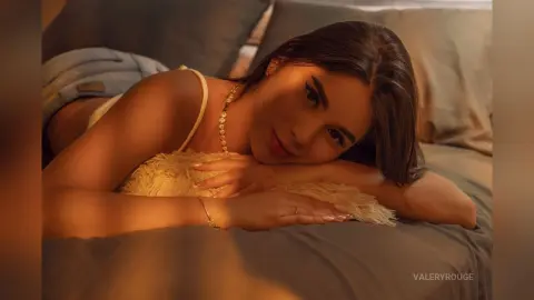 Young woman in a white fuzzy tank top relaxing on a bed in warm, cozy indoor lighting.